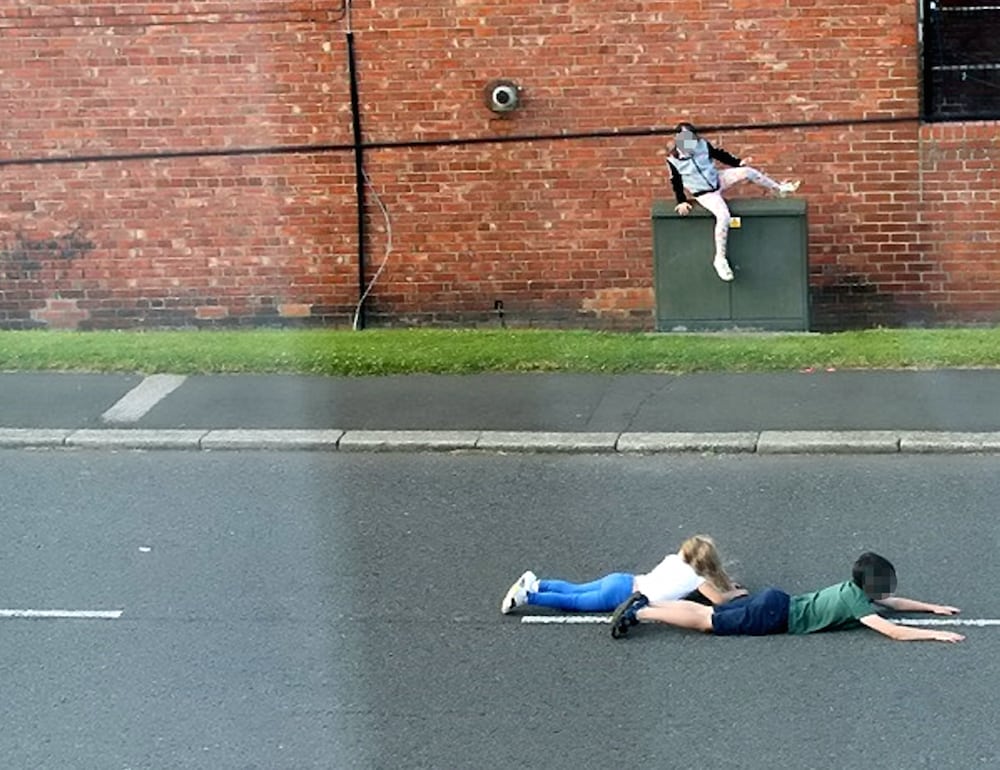 These shocking photographs show children dicing with death as they dodge cars by lying in the middle of a busy ROAD. See ROSS PARRY story RPYCHICKEN. The three children appear to be playing 'chicken', a game involving waiting as long as possible in the way of cars, before jumping away at the last second. In one of the images, two of the children are seen lying in the middle of the road, while another image shows one the children running out on to the road as a car speeds past. The photographs, which were taken in Washington, Tyne and Wear, were sent to police by local councillor Dianne Snowdon after local residents raised concerns. Officers from Northumbria Police are working to identify the children in the images so their parents can be spoken to about their reckless behaviour but police also want to remind people of the dangers of playing on and near busy roads.