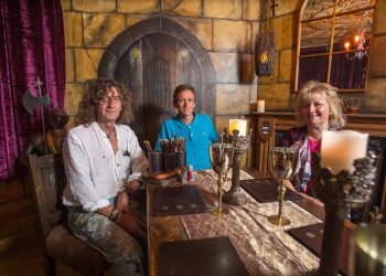 Local artist Martin Darcy, Jayne and Martin Townley. See SWNS story SWCASTLE; A quirky couple are living a real-life fairytale after turning their semi into a medieval CASTLE. Martin and Jayne Townley have painted the rear of the Weston-Super-Mare house to look like a grey stone fortress complete with battlements and archways over the windows. They have banners and flags flying from the guttering, a giant shield hanging on the outside and a pillory in the garden. Inside the house is like an old baronial hall with swords on the wall, gauntlets on the furniture and heavy purple drapes.