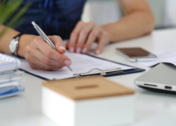 Close-up of female hands. Woman writting something and looking at mobile phone screen sitting at her office