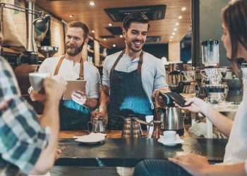 Smiling barista with barcore reader accepting smart phone payment