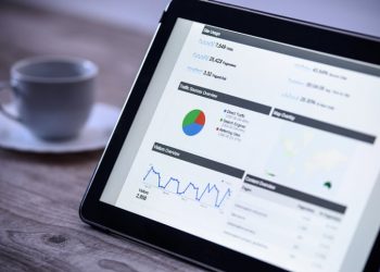 Charts and analytical data on the tablet screen with a cup of coffee on a wooden vintage table.
