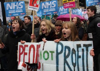Three young activists hold a 'people not profit sign'