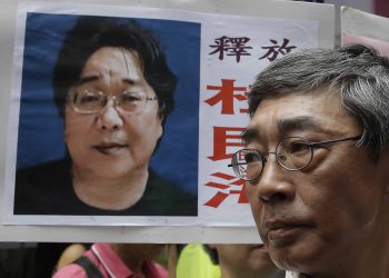 A picture of missing bookseller Gui Minhai is shown on a placard beside freed Hong Kong bookseller Lam Wing-kee, as the protesters are marching to the Chinese central government's liaison office in Hong Kong. A court in eastern China announced Tuesday, Feb. 25, 2020, that it has sentenced Gui, a naturalized Swedish citizen, to 10 years in prison. (AP Photo/Kin Cheung, File)