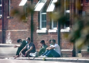 A group of men, thought to be migrants, sit outside in the sunshine after arriving yesterday night at Napier Barracks in Folkestone, Kent. Credit;PA