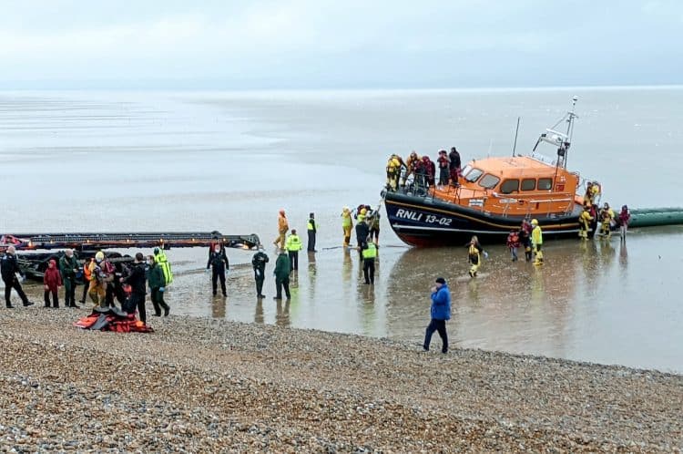 A lifeboat crew assist migrants from the English Channel in Dungeness, Kent. November 20, 2021. See SWNS story SWOCmigrants. Hundreds of migrants were rescued from the sea by RNLI lifeguards after crossing the Channel in small boats. Adults and young children wrapped in blankets were seen being led up the beach in Dungeness, Kent on Saturday (20/11). They were helped by lifeguards from RNLI Dungeness after attempting to seek asylum before the winter weather makes the journey too difficult. At least four dinghies packed with dozens of people reportedly reached the shore, as well as a lifeboat bringing in more from out at sea. Others arrived at Folkestone and Dover harbours, brought in by authorities. Border Force agents and police were on the scene as well as three coaches to pick the migrants up and take them to be processed.